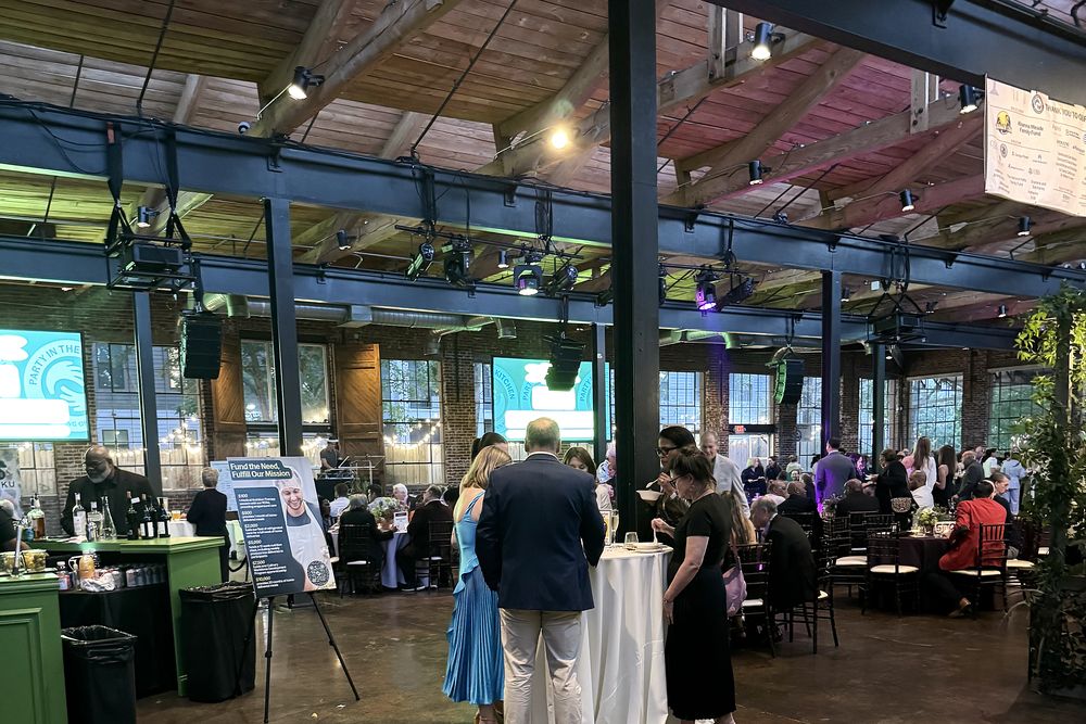 Guests at cocktail tables in front of event screens and a green bar