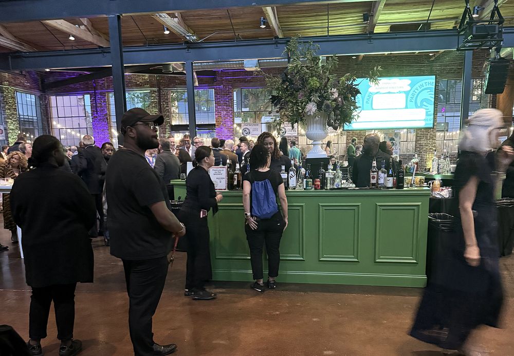 Guests and staff at a green bar beneath event screens