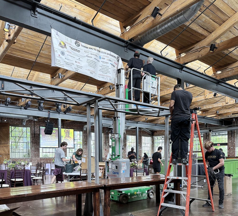 Crew installing equipment on a lift and ladder during setup day in a warehouse venue
